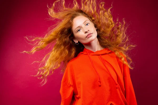 Retrato de uma linda menina ruiva com cabelo encaracolado voando olhando para a câmera em um fundo vermelho. — Fotografia de Stock