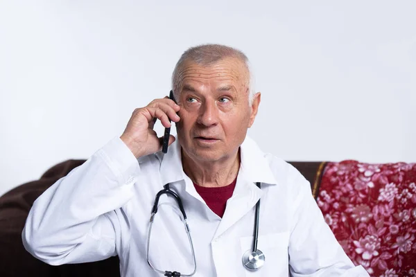 那位老医生戴着耳机，在讲电话。远程咨询和电子保健概念。一个医生的肖像。高级在线和大流行病概念. — 图库照片