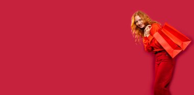 Banner, uzun format. Kırmızı arka planda kırmızı alışveriş torbaları taşıyan mutlu bir kız. Bir sürü boş alan var. Tatil ve alışveriş konsepti