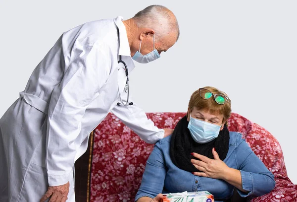 En gammal seriös läkare som bär mask kontrollerar en äldre kvinnas välbefinnande under en läkarundersökning hemma. Begreppet virus och pandemi — Stockfoto
