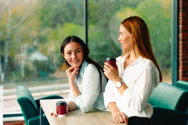 Coffee break. Business women drink coffee in a large modern office with large windows. They are waiting for the beginning of the meeting, making business decisions.