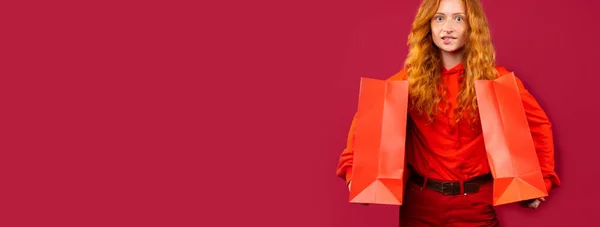 Banner, formato longo. Menina feliz segurando sacos vermelhos sobre fundo vermelho com muito espaço vazio. Conceito de férias e compras — Fotografia de Stock