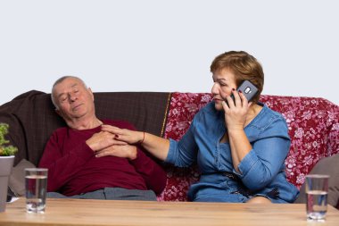Kadın telefonu tutar ve acil servisi arar, yaşlı kocası kanepede yatarken, erkek göğüs ağrısı, nefes darlığı hisseder. Son sınıf internet ve salgın konsepti.