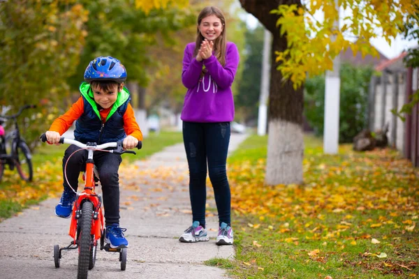 Brother and sister in the park. The boy learns to ride a bike alone. The sister in the background rejoices at his success. Photo on the background of autumn. High quality photo
