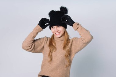 Tebessümlü beyaz arka plandaki kız şapkasını düzeltiyor ve yana bakıyor. Yüksek kalite fotoğraf