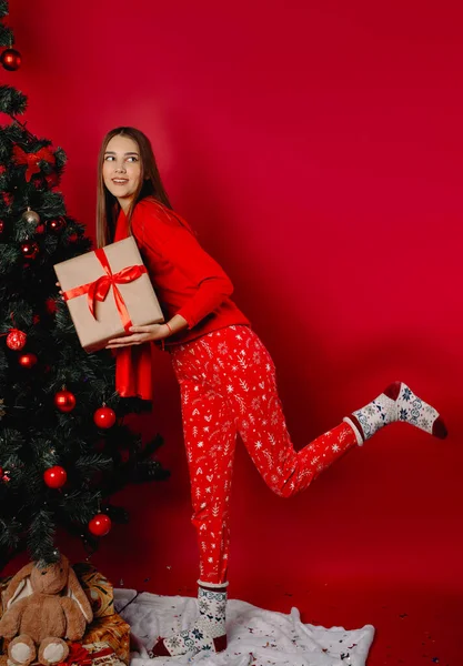 圣诞树旁一个可爱的女孩拿着一个礼品盒 望着别处 甜甜地笑着 高质量的照片 — 图库照片