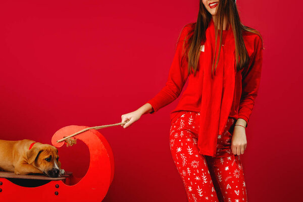 A girl in pajamas and a sad puppy on a sled. Photo on a red background. Christmas. High quality photo