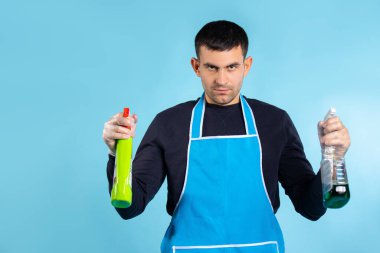Ciddi bir bakışı olan, eline sprey sıkmış, kameraya bakan bir adam. Mavi arka planda bir fotoğraf. Cinsiyet klişeleri kavramı. Yüksek kalite fotoğraf