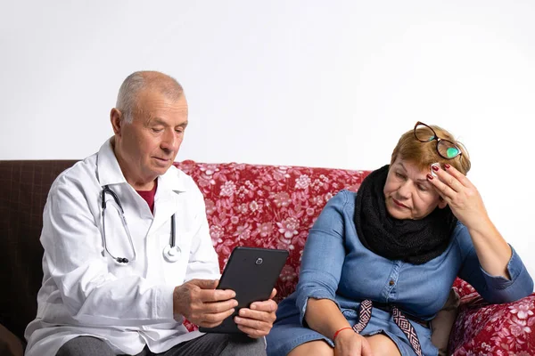 The family doctor came home to an elderly woman. After checking, the doctor reads the diagnosis from the tablet. High quality photo