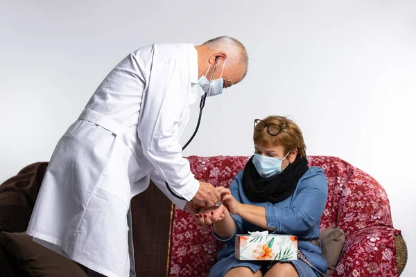 Maskeli bir doktor yaşlı bir kadının nabzını evde muayene ederken ölçer. Virüs ve salgın hastalık konsepti. Yüksek kalite fotoğraf