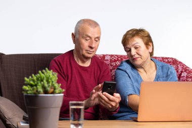 Karantina sırasında geçirilen zaman. Yaşlı çift evde bilgisayar ve telefon başında kanepede oturuyor. Yüksek kalite fotoğraf