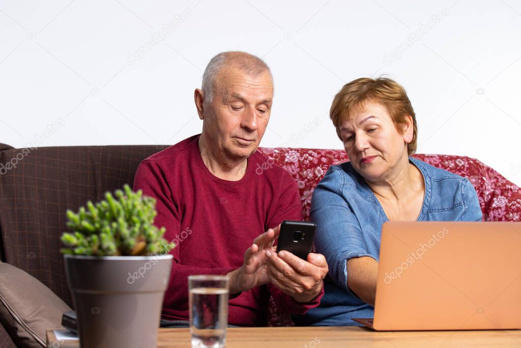Time spent during quarantine. The older couple are sitting at home on the couch at the computer and telephone. High quality photo
