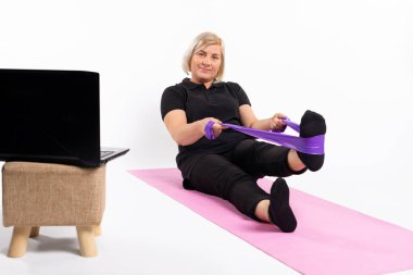 Senior woman on the rug, doing exercises with an elastic band. Online training during quarantine. High quality photo