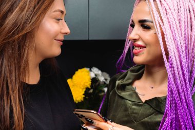 Mutfaktaki akıllı telefonlu kız arkadaşlarının portresi. Birbirlerinin gözlerine tatlı tatlı bakıp gülümserler. Yüksek kalite fotoğraf