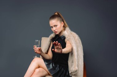 Ciddi genç iş kadını, kürklü, elinde bir bardak şampanyayla gri arka planda duruyor. Yüksek kalite fotoğraf