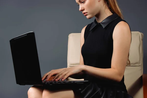 Foto ingrandita di una signora seria con un computer portatile su una sedia su uno sfondo grigio. Lavoro online a casa, concetto di pandemia — Foto Stock