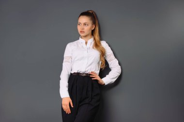 Businesswoman posing to camera and looking to the side on a gray background with empty side space for advertisment. High quality photo