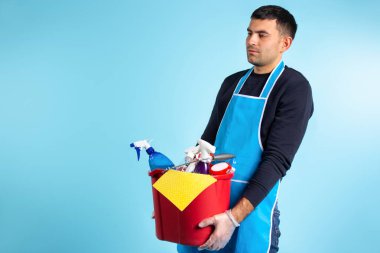 Bir adamın elinde bir kova dolusu temizlik malzemesi var. Cinsiyet eşitliği. Mavi arka plan, yan boşluk. Yüksek kalite fotoğraf