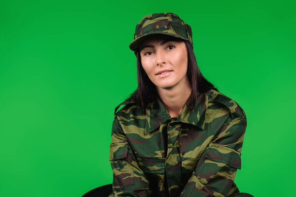 Portrait of a cute woman in military uniform on a green background with side space for advertisment. High quality photo