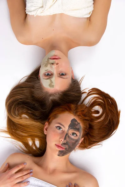 Yüzünün yarısına maske takmış iki kız yerde yatıyor. Sağlıklı ten ve güzellik kavramı. Yukarıdan bir fotoğraf. Yüksek kalite fotoğraf