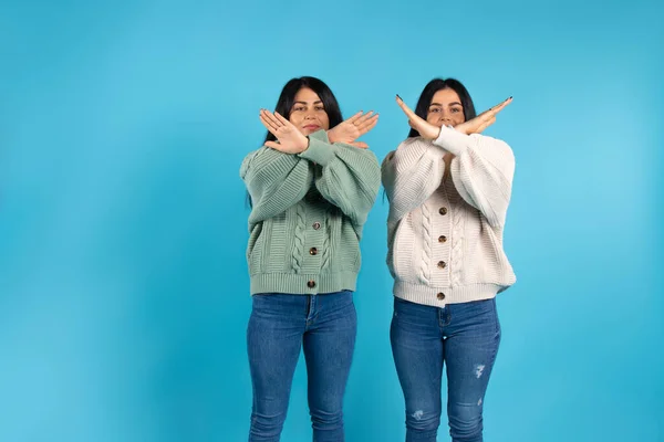 Tvillingar, brunetter i samma kläder på en blå bakgrund, korsade armarna, visar stopp. Sidoutrymme. — Stockfoto