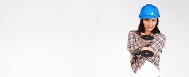 Banner, uzun format. Sert şapkalı bir kadın beyaz arka planda öğütücü disklerle poz veriyor. İnşaat ve cinsiyet kavramı