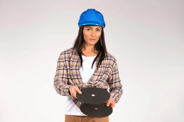 Una manitas con un sombrero duro sostiene un disco abrasivo para amoladora. Constructora. Fondo blanco. — Foto de Stock