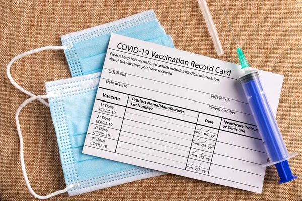 Рекордні картки для вакцинації від коронавірусу. Хірургічна маска розділена на дві частини та шприц. Концепція перемоги Ковіда-19 — стокове фото