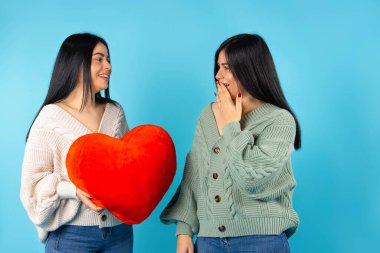 Mavi arka planda kırmızı kalpli mutlu ikizler gülümsüyor ve şaşırıyorlar..