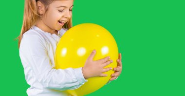 Sancak- uzun format. Küçük bir kızın yeşil arka planda aydınlatıcı bir renk balonunu ısırmaya çalışırken çekilmiş yakın plan fotoğrafı. Yüksek kalite fotoğraf