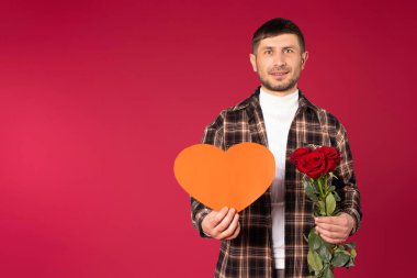 Elinde kırmızı kağıt bir kalp ve bir buket kırmızı gülle genç bir adamın portresi. Sevgililer Günü. Boş alanı olan kırmızı arkaplan. Yüksek kalite fotoğraf