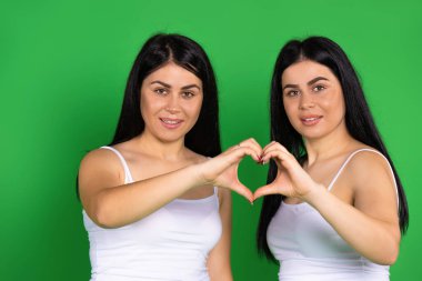 Yeşil arka plandaki ikiz kardeşler ellerini kalp şeklinde tutuyorlar. Aşk, hayırseverlik, Sevgililer Günü konsepti. Yüksek kalite fotoğraf
