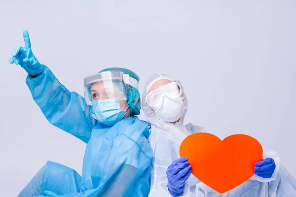 Genç bir doktor büyük kırmızı kağıt kalbi kameraya tutarken hemşirenin işaret parmağıyla sırt sırta oturuyor. Yüksek kalite fotoğraf
