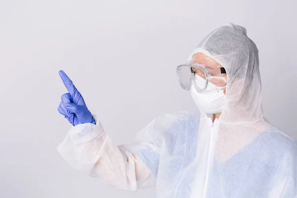 Profile photo. A doctor in protective gear points with his index finger to the side on a white background. High quality photo