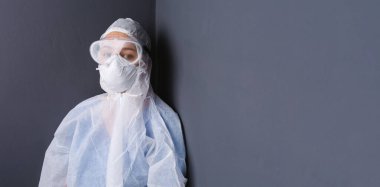 Pankart. Koruyucu tulumlu, gri duvarlı, yan tarafı geniş bir doktor. Koronavirüsle mücadele kavramı. Yüksek kalite fotoğraf