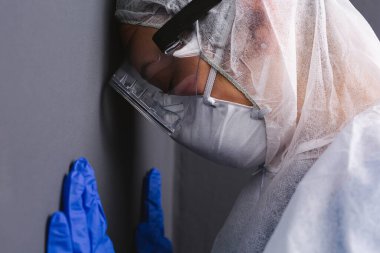 Koruyucu ekipmanlı bir doktor alnını ve ellerini gri bir duvara bastırıyor. Koronavirüsle uğraşırken yorgunluk. Yüksek kalite fotoğraf