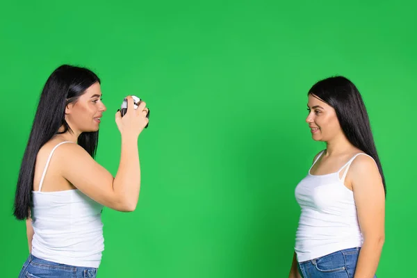 Сестры позируют и фотографируют на винтажную камеру. Зеленый фон с пустым пространством. — стоковое фото