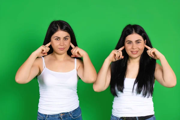 Os gêmeos cobrem seus ouvidos com seus dedos indicadores contra um fundo verde. — Fotografia de Stock