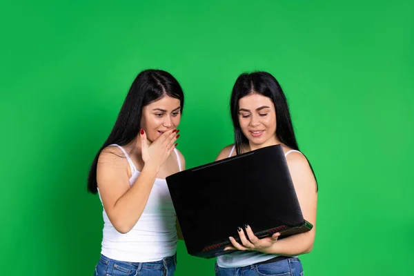 Surprised girls with laptop on a green background. Pastime concept. — Stock Photo, Image