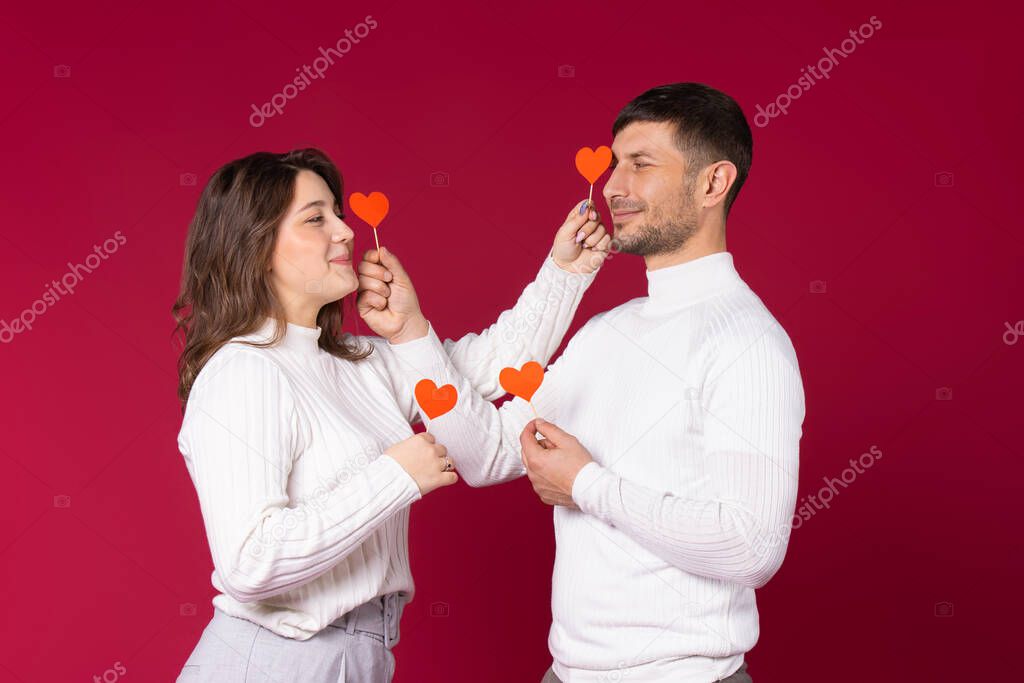 A loving couple posing with red paper hearts on red background. Spending time on St.Valentines Day.