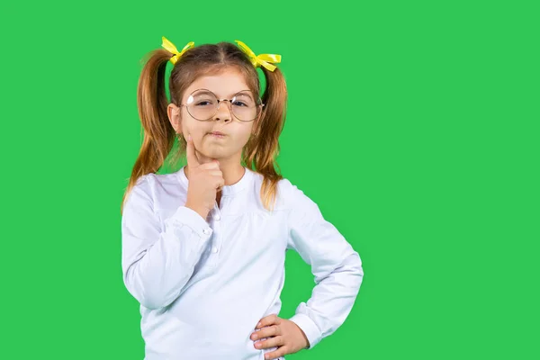 Une fille chère avec des queues de cheval et des lunettes tient sa main sur son visage et regarde la caméra. Fond vert et espace latéral. — Photo