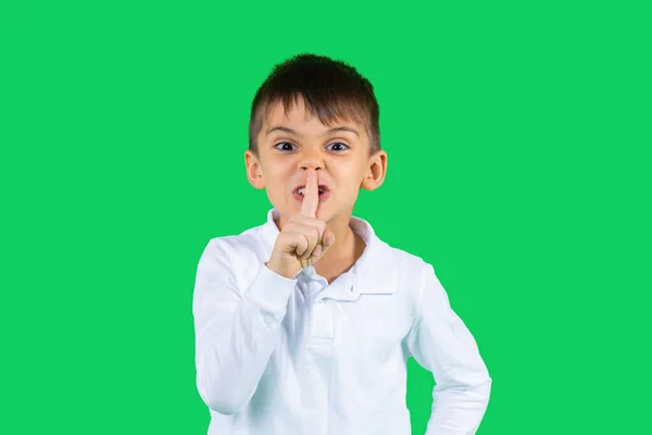 Un colegial con una camisa blanca muestra su dedo índice en silencio y mira a la cámara. Fondo verde. Espacio lateral. — Foto de Stock