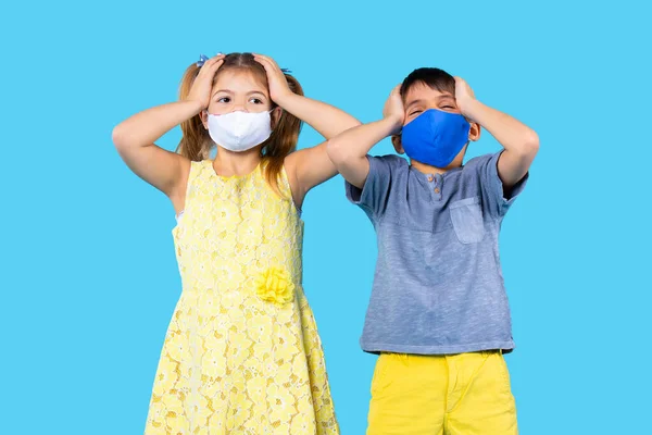 Los niños en edad preescolar con máscaras protectoras sostienen la cabeza con las manos sobre un fondo azul. Concepto de protección antivirus. — Foto de Stock