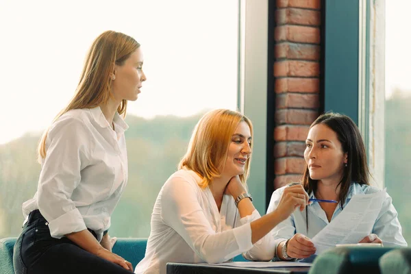 Genç kadın girişimciler büyük pencereli bir ofiste otururken yeni bir projeyi tartışıyorlar.