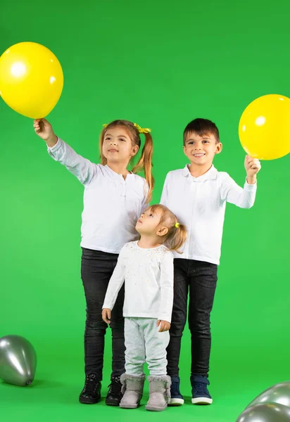 Kinderen van verschillende leeftijden op een groene achtergrond met ballonnen. Oprechte emoties concept. — Stockfoto