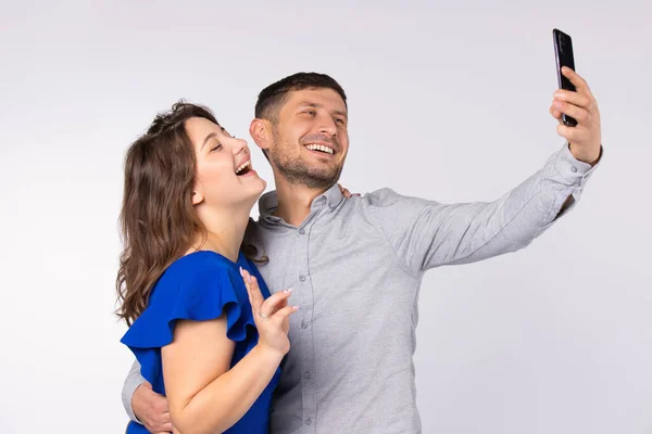 Feliz joven pareja sonriente abrazándose y tomando selfie en el teléfono inteligente. Signo de paz sobre fondo gris. —  Fotos de Stock