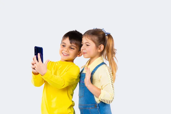 Lindos niños con teléfono inteligente hablar sobre la comunicación de vídeo sobre fondo blanco. La chica agita su mano en saludo. —  Fotos de Stock