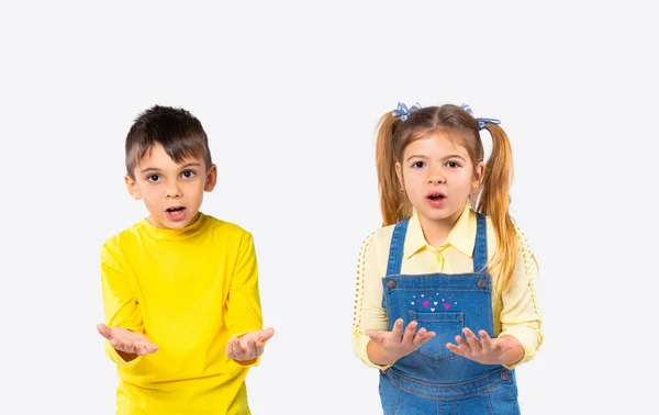 Los niños preescolares sorprendidos miran a la cámara con los brazos extendidos. Fondo blanco y concepto de emoción. — Foto de Stock