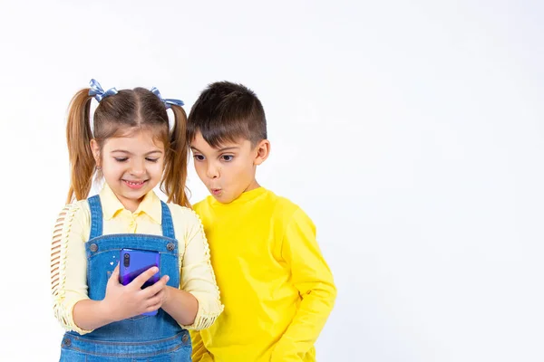 Los niños en edad preescolar están viendo algo en un smartphone. Un chico con una cara sorprendida. Fondo blanco y espacio lateral. — Foto de Stock