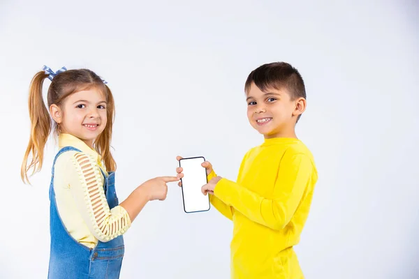 Enfants mignons posant avec un smartphone montrant l'écran lumineux. Fond blanc. — Photo